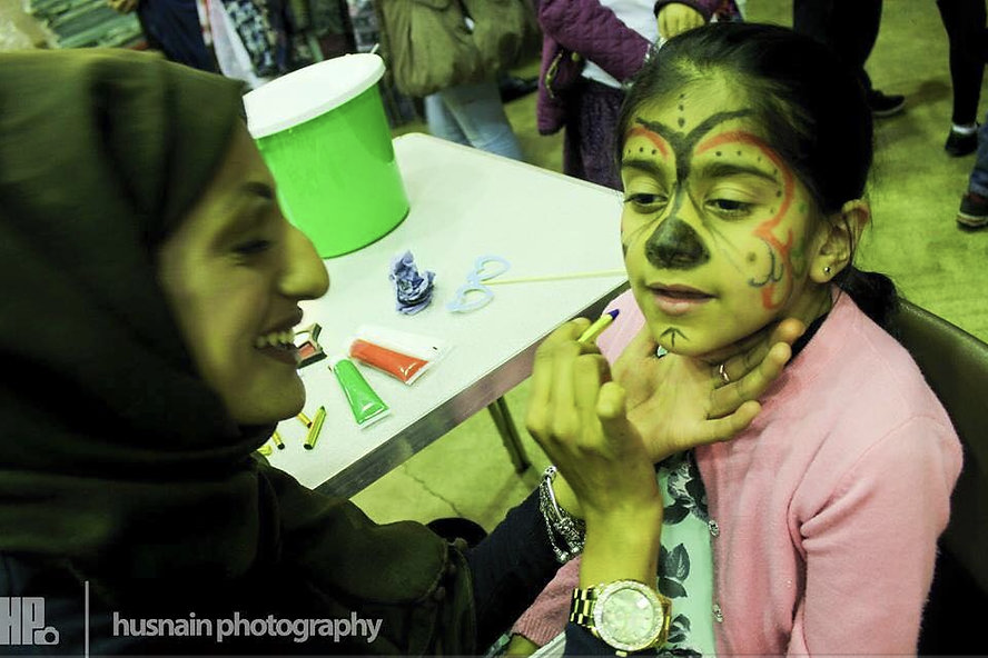 A woman painting a young girl's face as a butterfly.